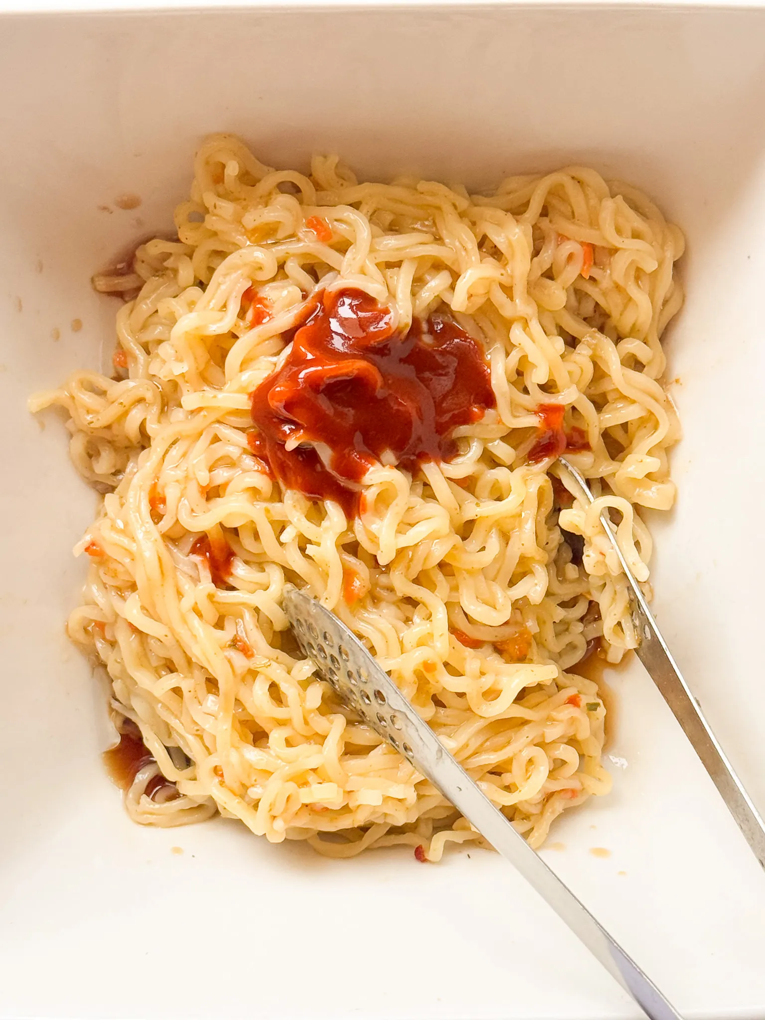 Adding the sauces and the sesame oil to the noodles.