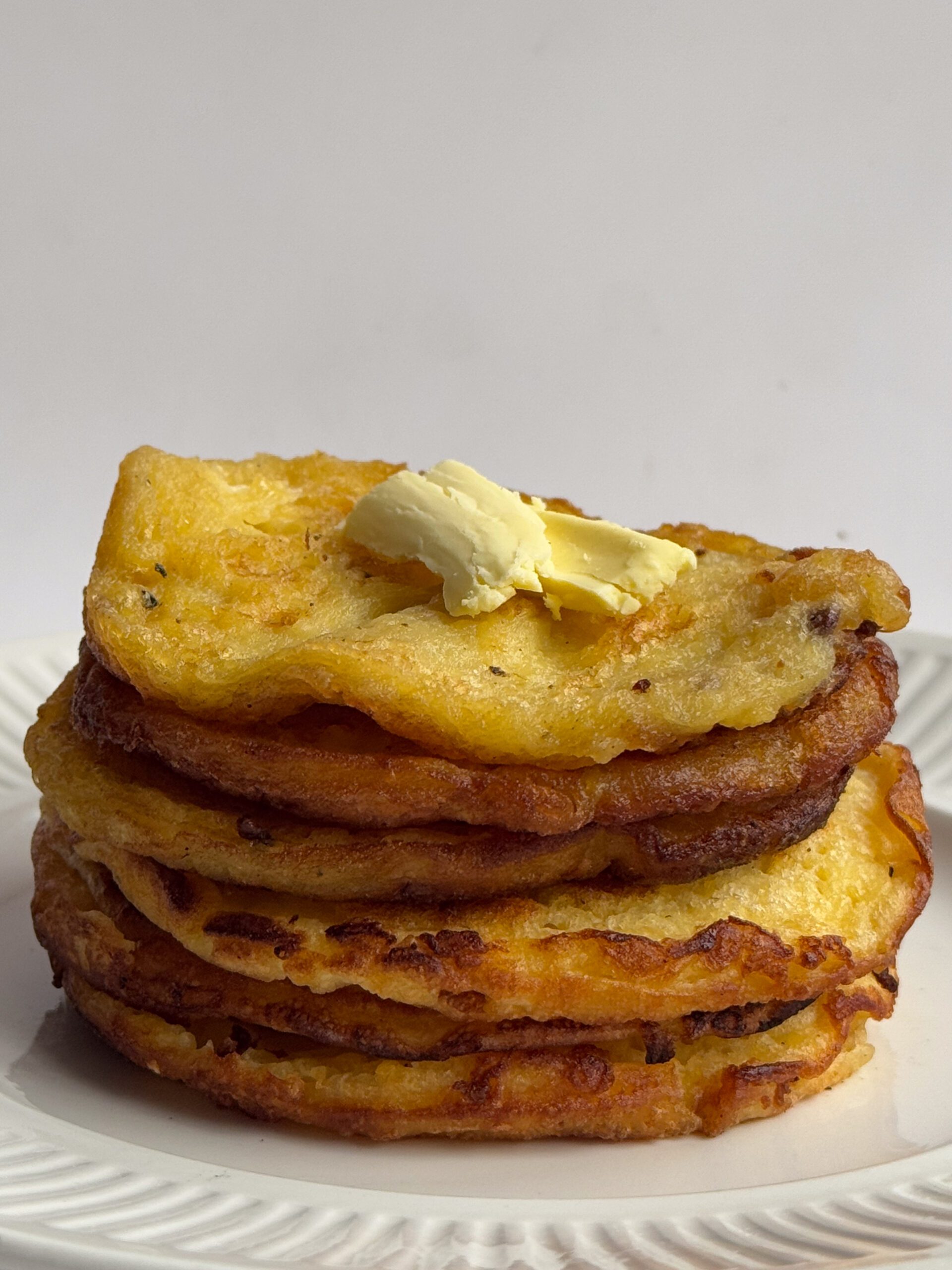 A stack of fresh pancakes with butter scoop on top.